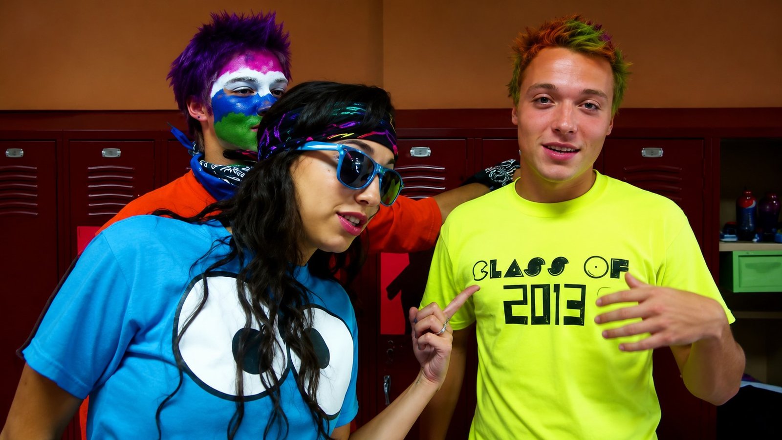 Three American high-school students in face paint and sunglasses in front of red lockers
