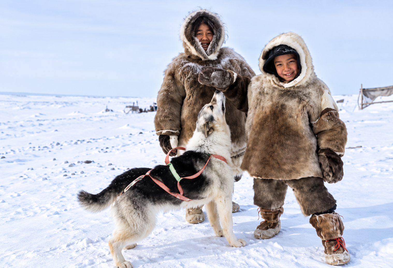 Picture 3 — two people in fur parkas standing in the snow with a sled dog.